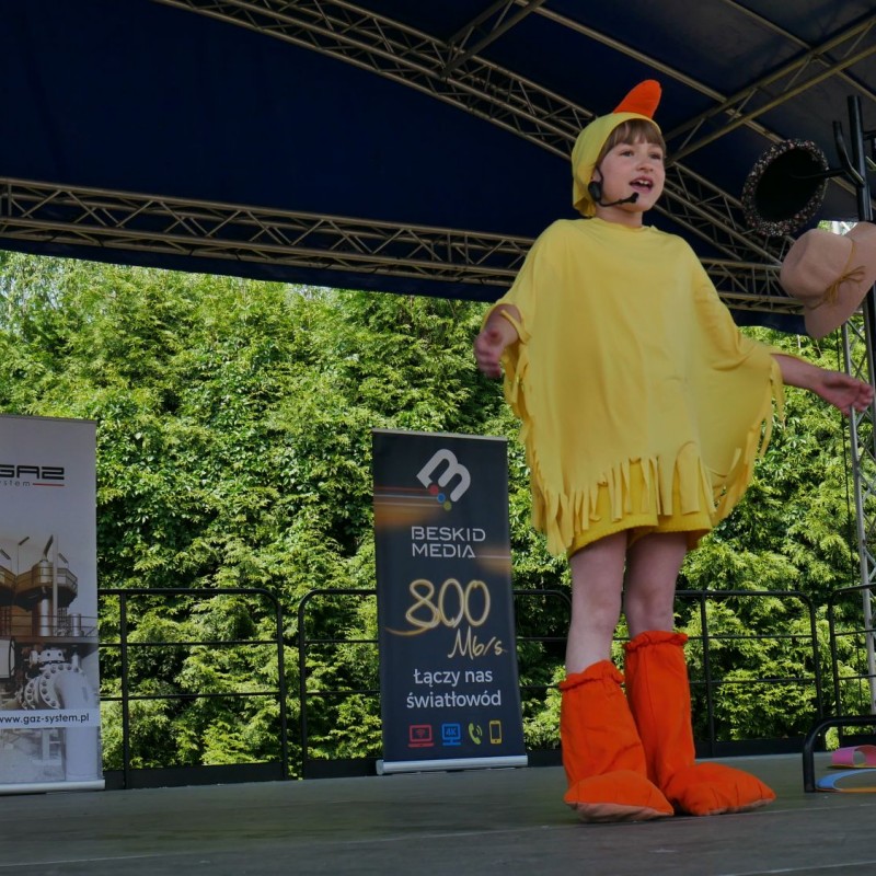 Dziewczynka przebrana za żółtego kurczaka na scenie plenerowej.