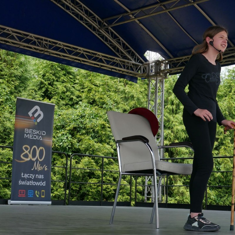 Dziewczynka w czarnym kostiumie stoi przed krzesłem podczas występu na scenie.