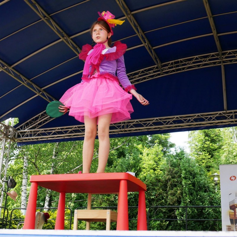 Dziewczynka w różowym stroju podczas występu stoi na stole.