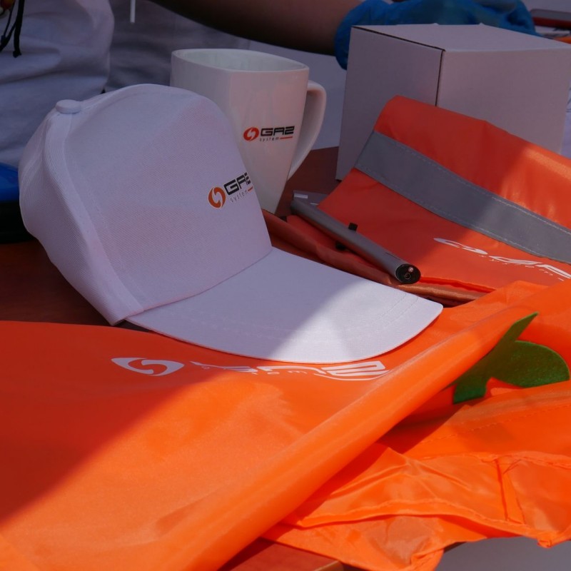 Zbliżenie na pomarańczowe hustki oraz białe czapki z logo „Gaz system”.