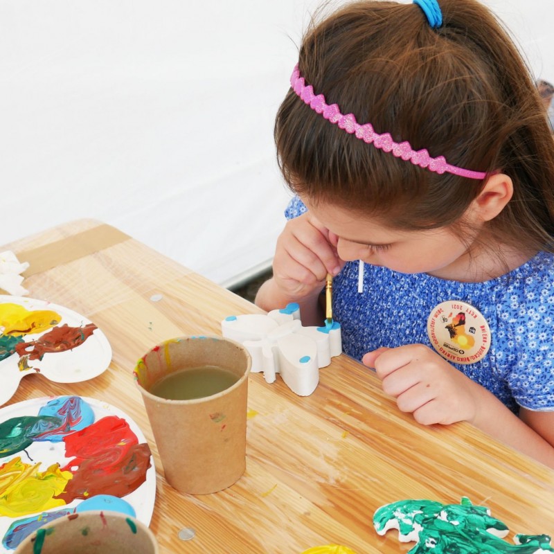 Dziewczynka wykonuje pracę plastyczną za pomocą farby malując figurki.