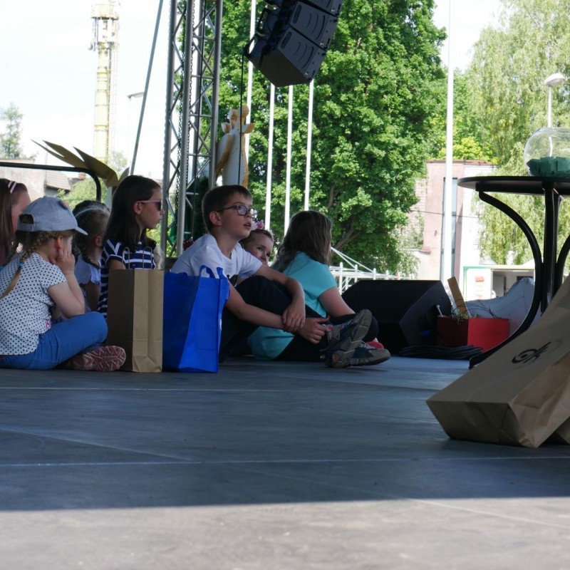 Dzieci siedzą na scenie otoczone paczkami.