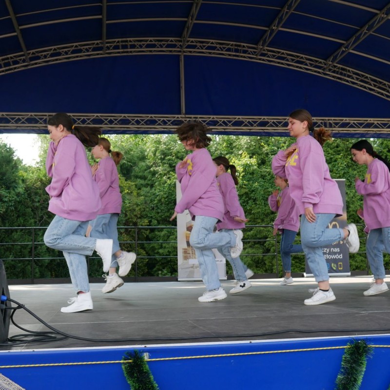Dziecięca grupa taneczna w różowych bluzach podczas występu na scenie plenerowej.