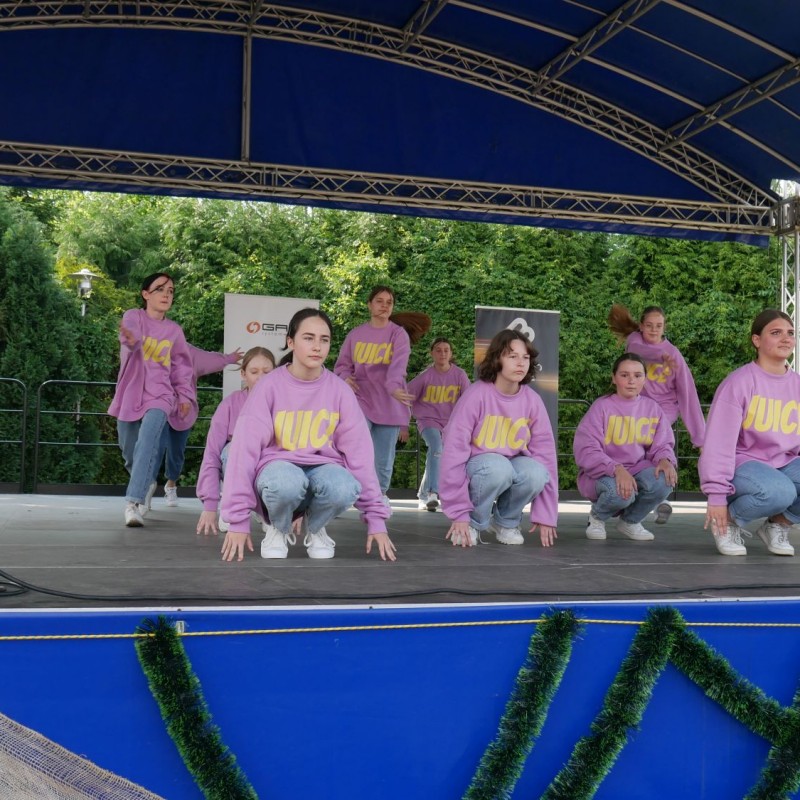 Dziecięca grupa taneczna w różowych bluzach podczas występu na scenie plenerowej.