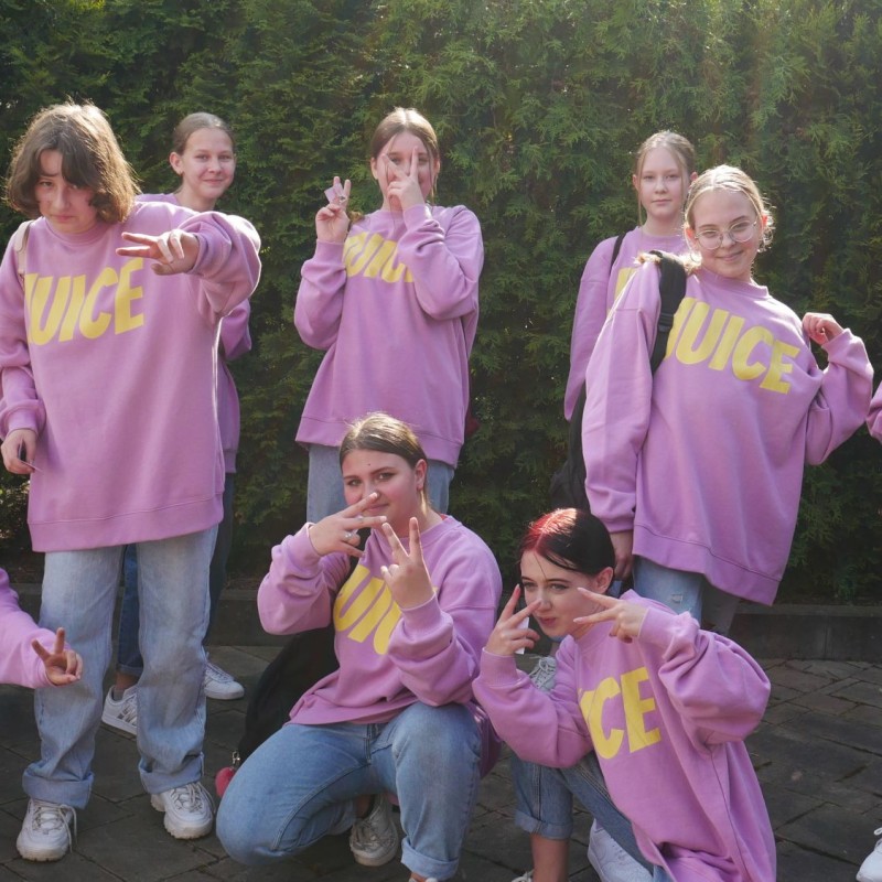 Grupa taneczna w różowych bluzach pozuje do zdjęcia.
