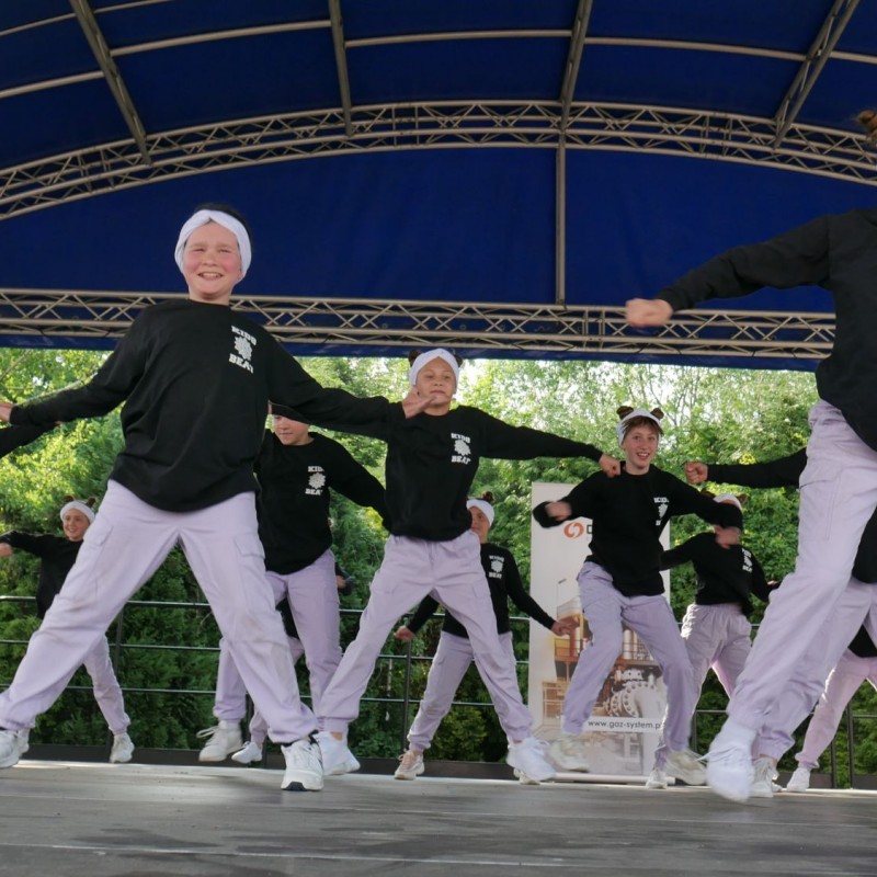 Grupa taneczna w czarnych bluzach podczas występu na scenie plenerowej.