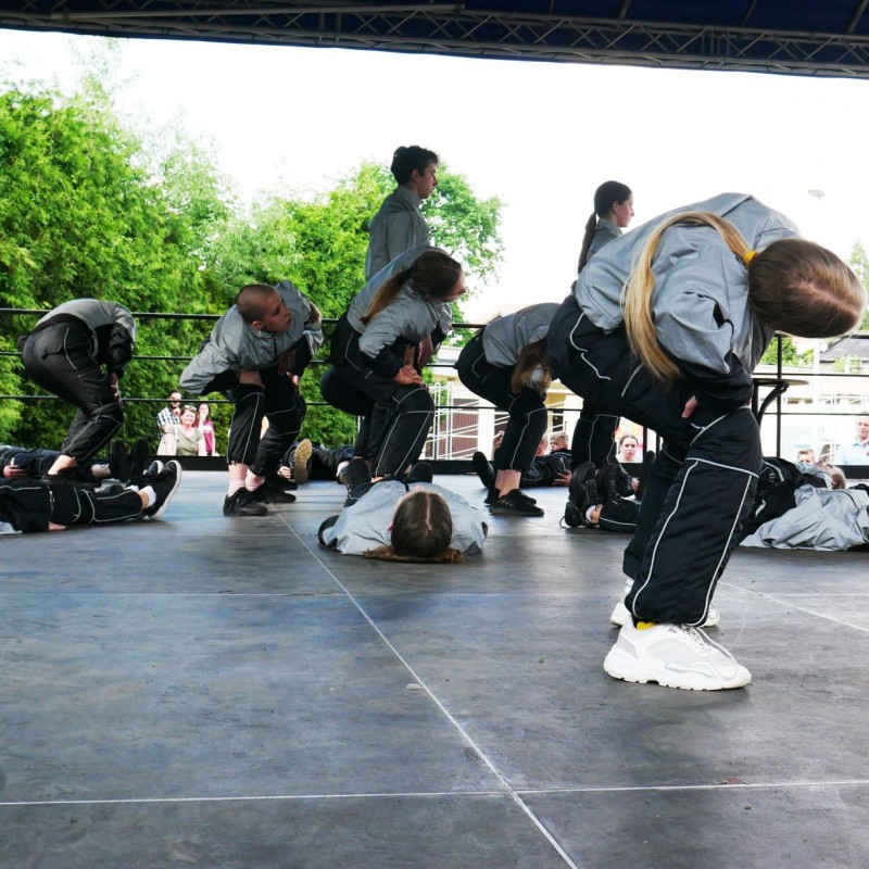 Grupa taneczna podczas występu na scenie plenerowej, są ubrani w szare bluzy.