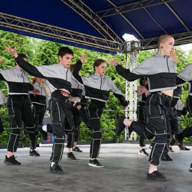 Grupa taneczna w beżowych bluzach podczas występu na scenie plenerowej.