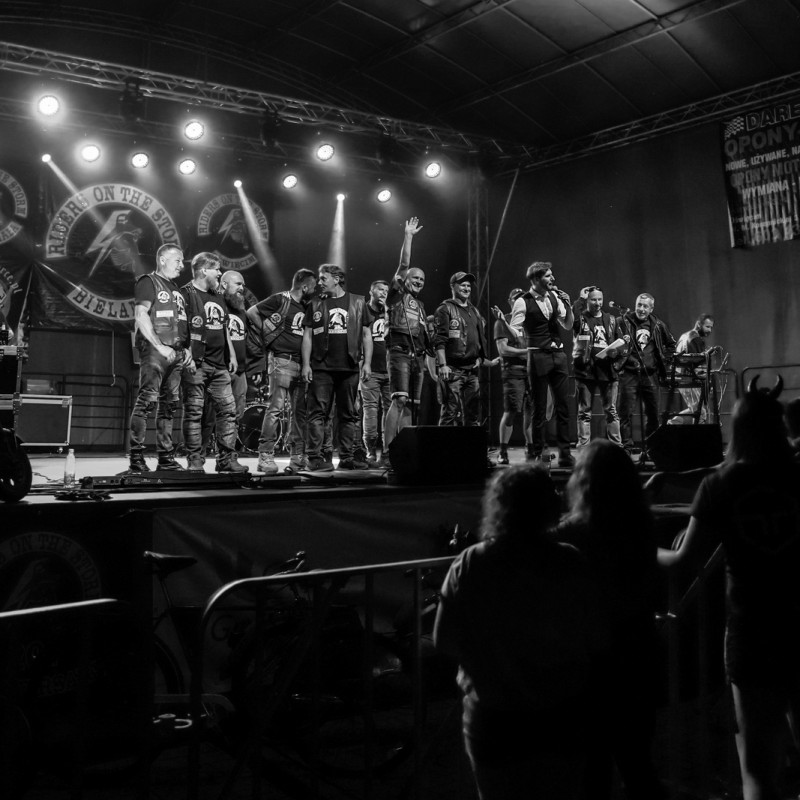 Czarno-białe zdjęcie, grupa motocyklowa „Riders of the storm” wieczorem na scenie plenerowej.