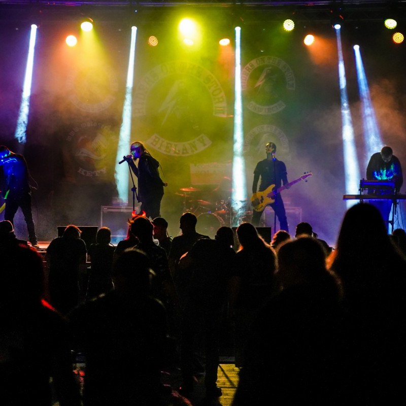Muzycy podczas występu oświetleni na scenie plenerowej, przed scena ludzie.
