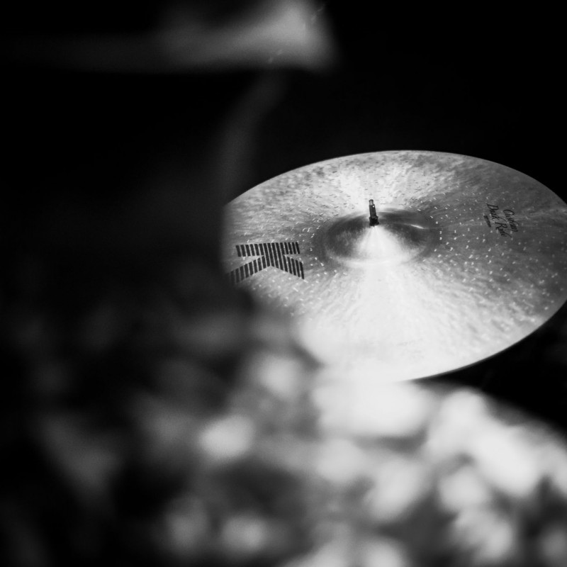 Czarno-białe zdjęcie, zbliżenie na perkusję zza pleców perkusisty.
