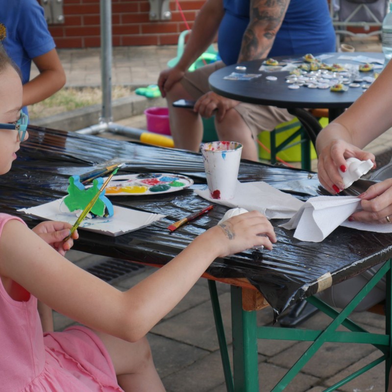 Dziewczynka z kobietą wykonują pracę plastyczną farbami przy stole.