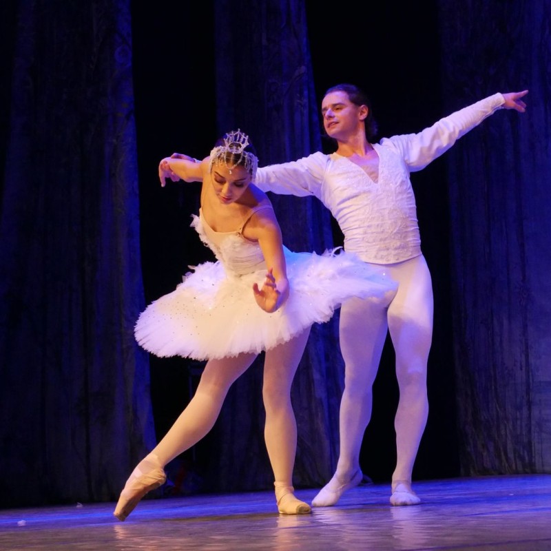 Baletnica w białej sukni w ukłonie, za nią tancerz z rozpostartymi rękoma również ubrany na biało.