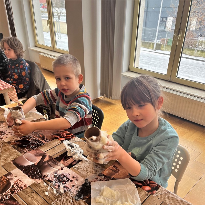 Dzieci dekorują rolki po papierze materiałami i innymi plastycznymi materiałami.