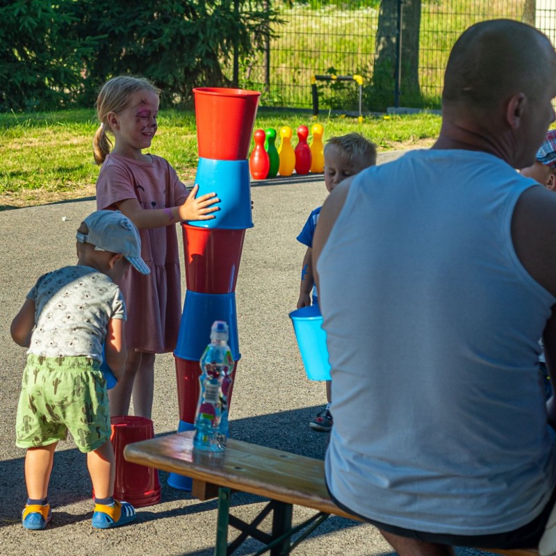 Fot. Łukasz Kuc/Dziewczynka układa wieżę z czerwonych i niebieskich wiaderek, małe dzieci przyglądają się jej. Dziewczynka ma pomalowaną twarz.