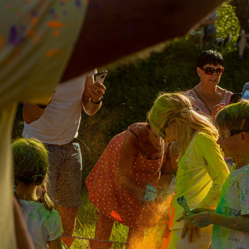 Fot. Łukasz Kuc/Grupa osób częściowo ubrudzonych kolorowym proszkiem, dziewczynka strzepuje z siebie pomarańczowy pył.