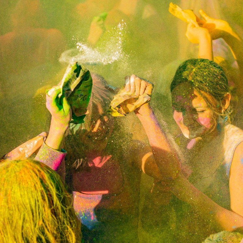 Fot. Łukasz Kuc/Uśmiechnięte dziewczyny rzucające kolorowym proszkiem w kłębach dymu na festiwalu kolorów.