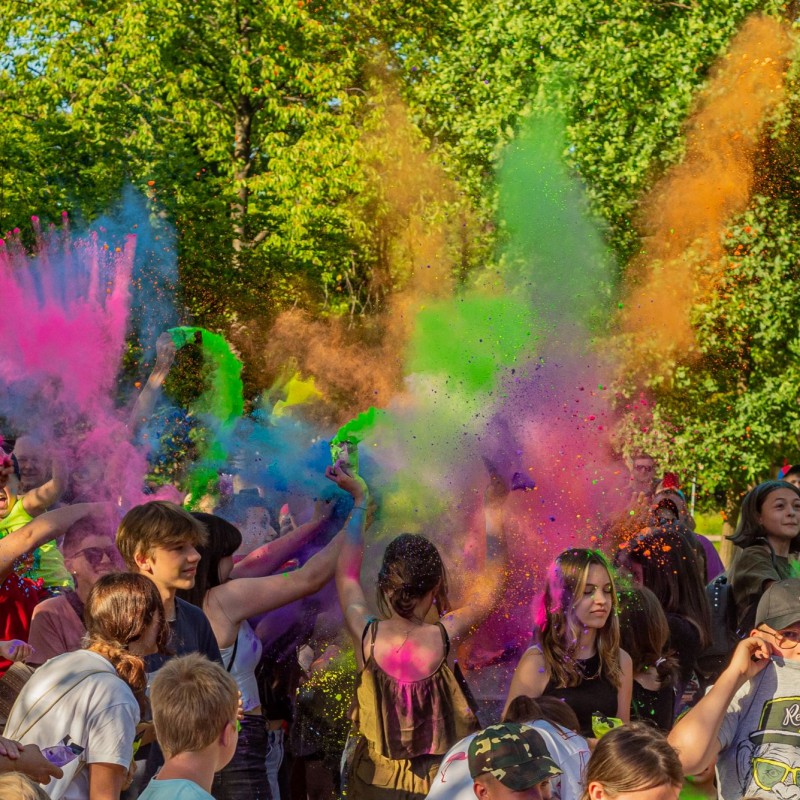 Fot. Łukasz Kuc/Festiwal kolorów, grupa ludzi wyrzuca w górę różnobarwny proszek. 