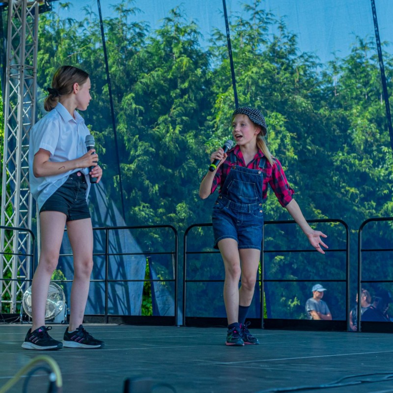 Fot. Łukasz Kuc/Dziewczynki stoją na scenie plenerowej, jedna z nich śpiewa do mikrofonu wykonując gest.