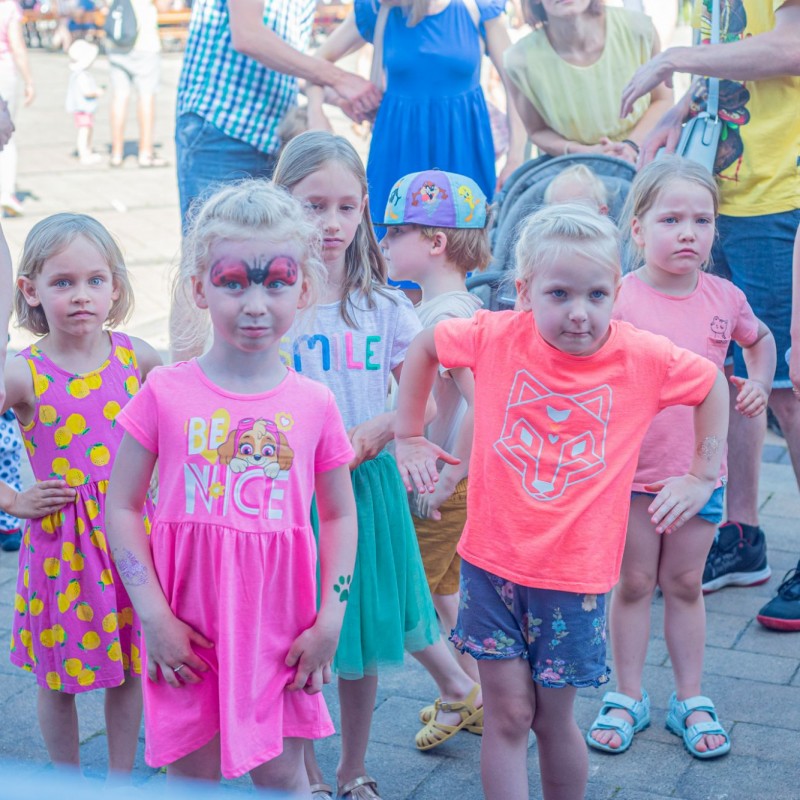 Fot. Łukasz Kuc/Małe dzieci pośród grupy dorosłych wykonują ruchy na placy przed domem kultury.