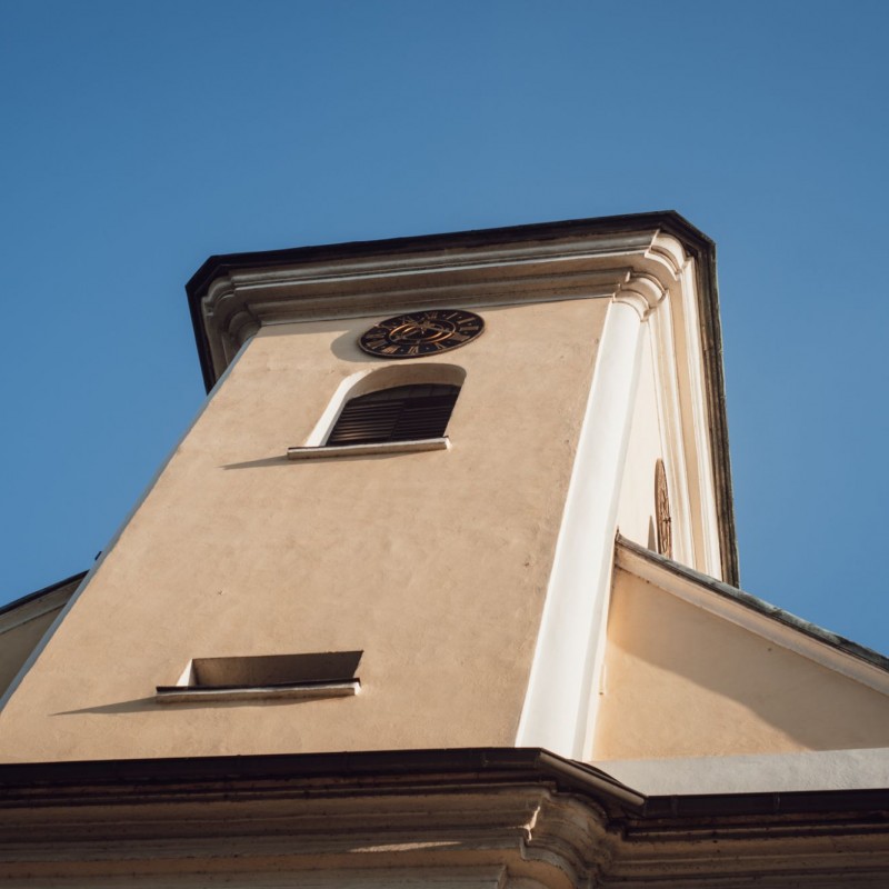 Fot. Łukasz Kuc/Beżowa wieża kościelna z zegarem sfotografowana od dołu w bezchmurny dzień.