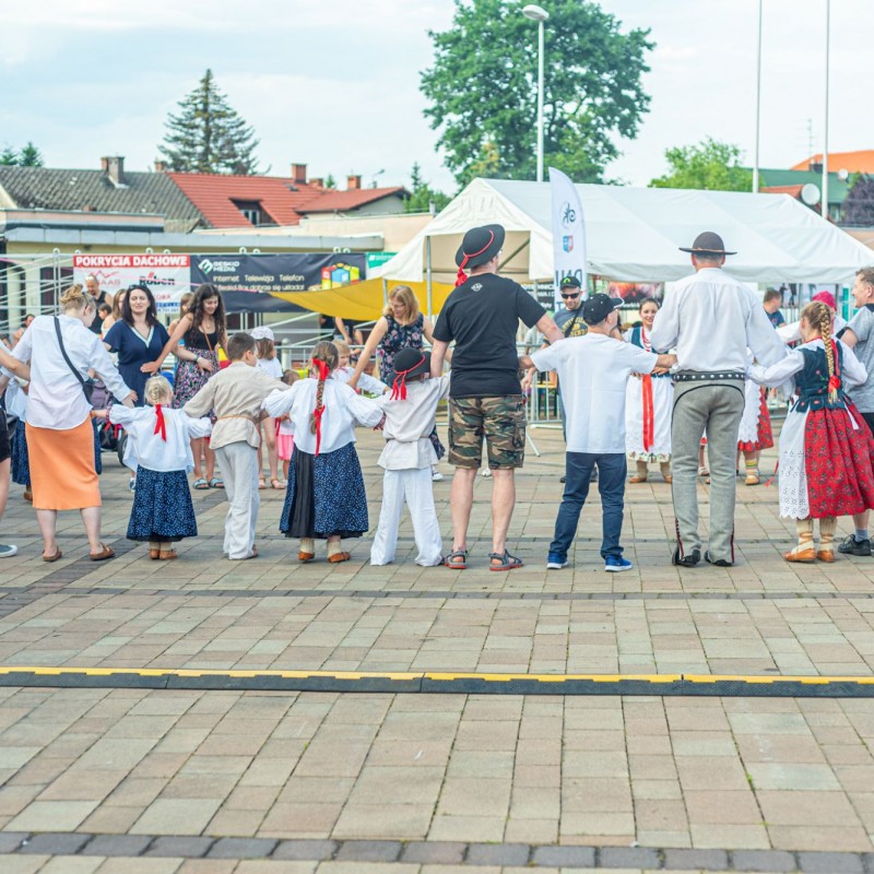 Fot. Łukasz Kuc/Ludzie uczestniczą w zabawie na placu domu kultury, ustawieni są w okrąg trzymając się za ręce.