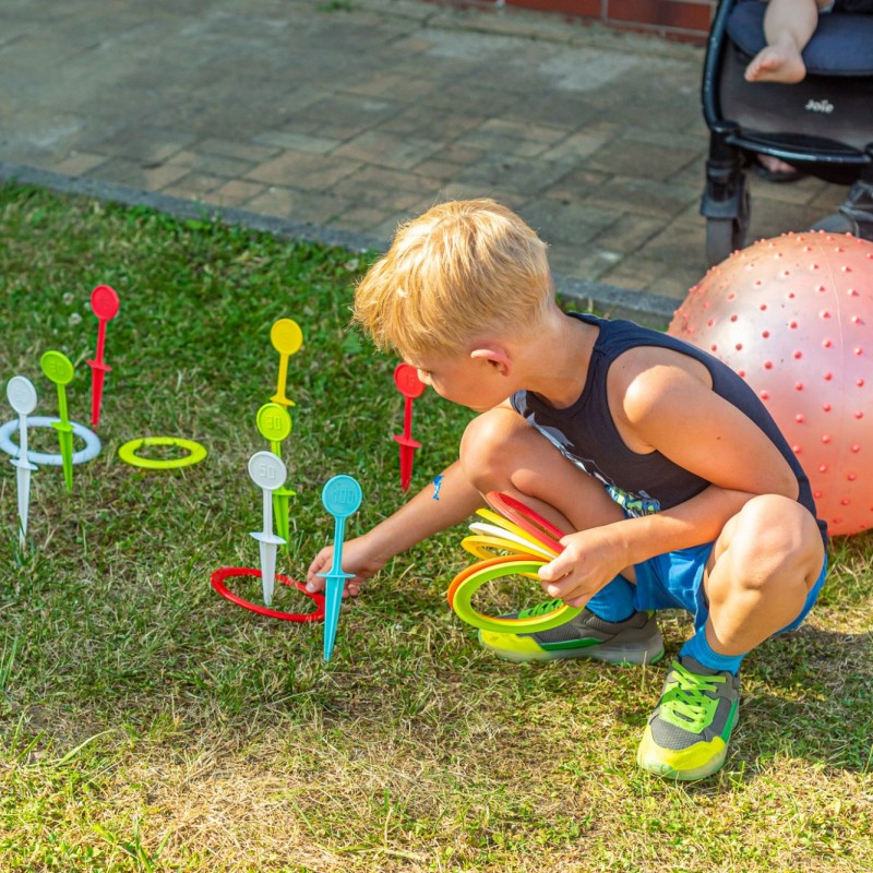 Fot. Łukasz Kuc/Chłopiec nakłada kolorowe, plastikowe krążki na wbite w trawę zabawkowe paliki.