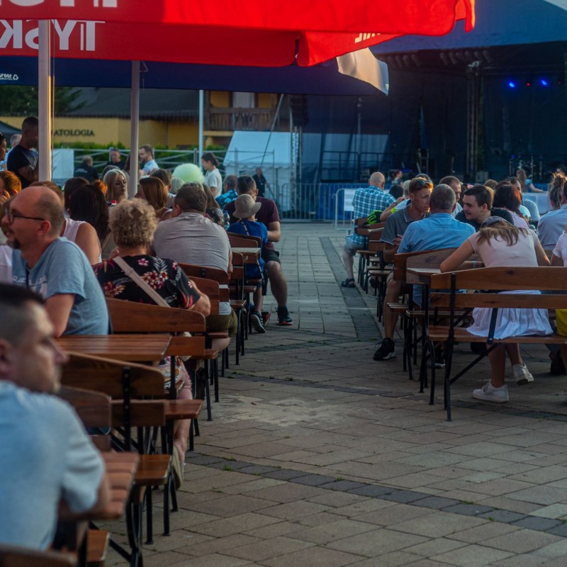 Fot. Łukasz Kuc/Ludzie siedzą przy ustawionych stolikach z ławkami pod baldachimem na placu domu kultury.