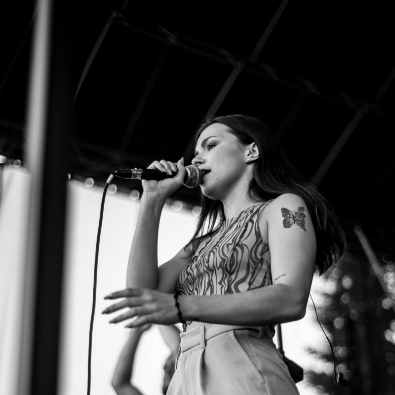 Fot. Łukasz Kuc/Czarno- białe zdjęcie wokalistki trzymającej mikrofon występującej na scenie.