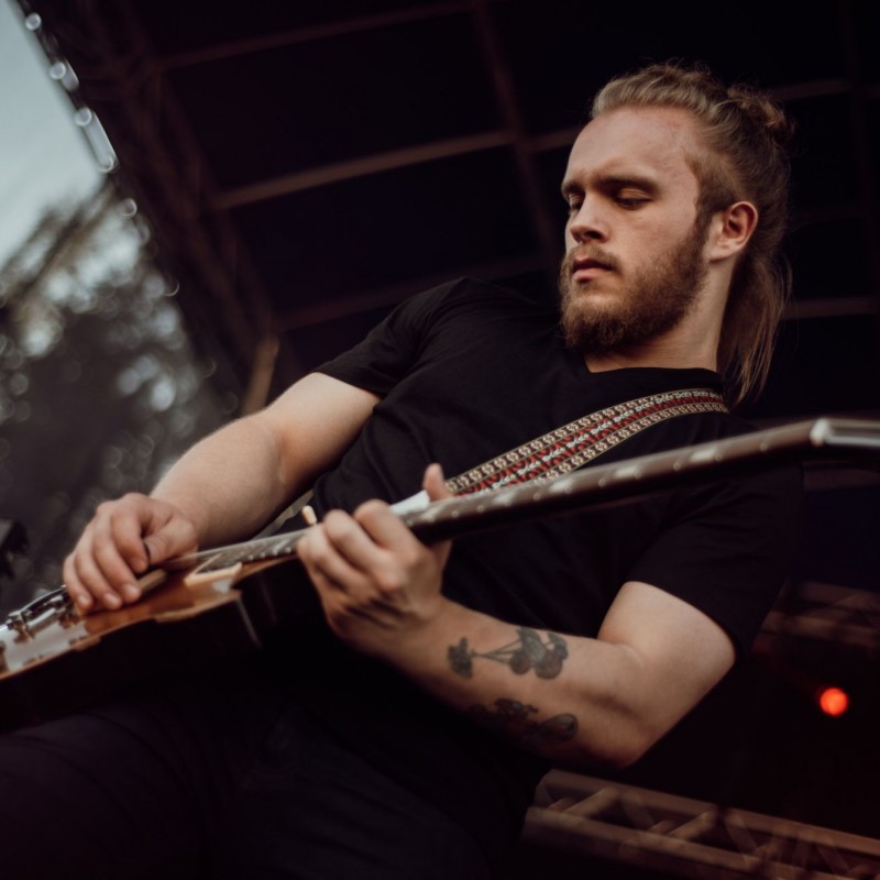 Fot. Łukasz Kuc/Gitarzysta w czarnej koszulce podczas występu na scenie plenerowej.