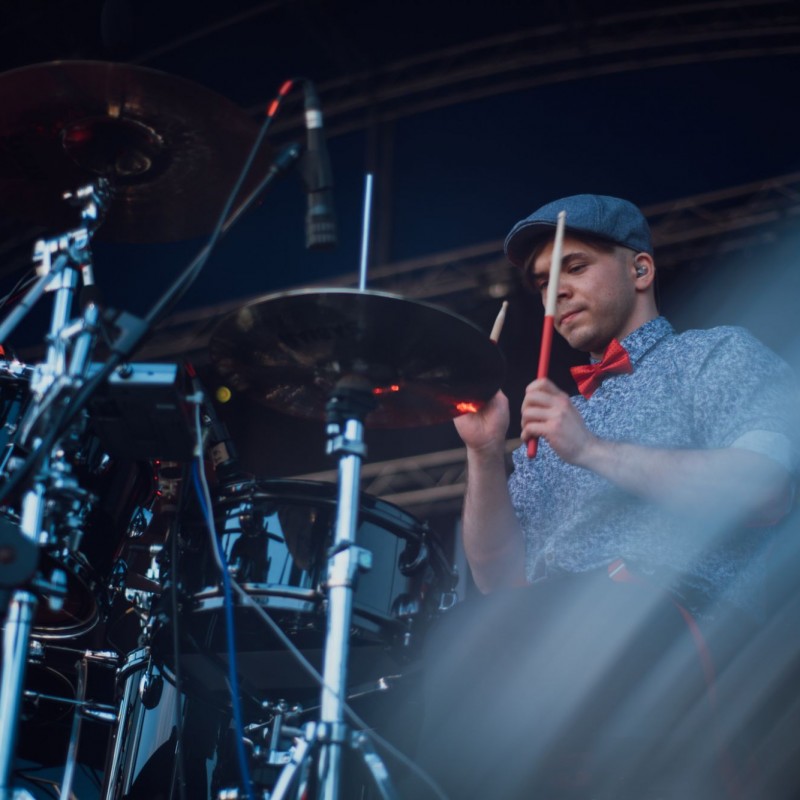 Fot. Łukasz Kuc/Perkusista podczas gry ubrany w koszulę ze wzorkami, beret i czerwona muszkę.