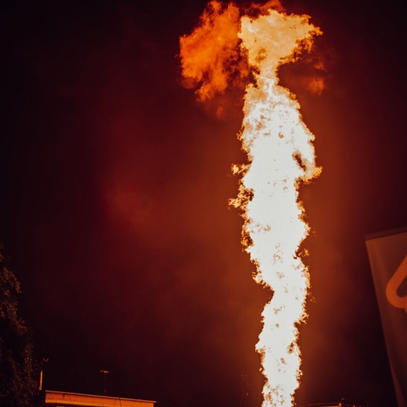 Fot. Łukasz Kuc/Słup ognia na tle ciemnego nieba, z boku chorągiewka promująca firmę Beskid Media.